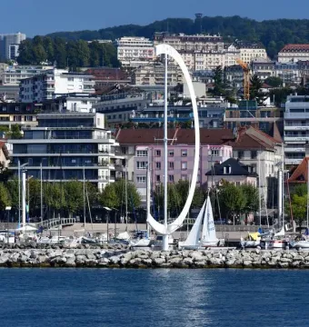 Éole, a large white curved sculpture on a rocky breakwater beside sailboats in a marina.
