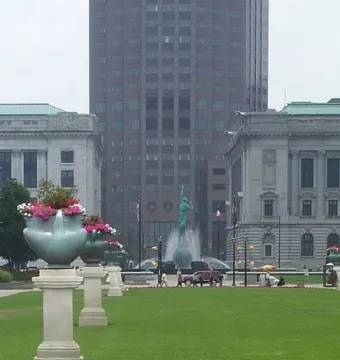 Fountain of Eternal Life in a downtown plaza with water spraying between two stone buildings and a tall skyscraper nearby.