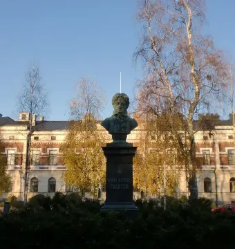 Frans Michael Franzén monument on a tall pedestal beside shrubs and trees in front of a grand building.