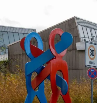 The Boxers sculpture with a bright blue and vivid red figure standing on a dark base outdoors.