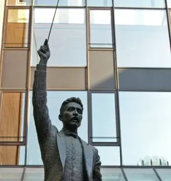 A Lluís Millet bronze statue holding a conductor’s baton aloft on a stone pedestal.