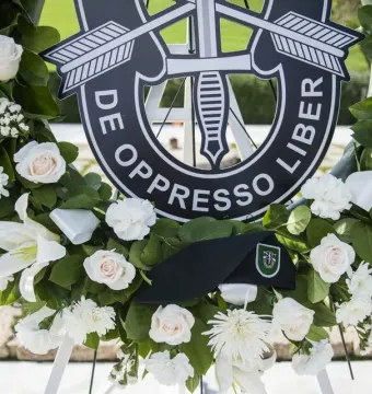 A memorial wreath with white and pale pink flowers, centered on a black Special Forces emblem and a black beret at America\'s Response Monument.