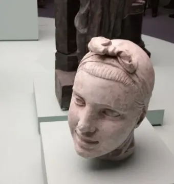 Head sculpture of Girl with an Oar with a decorative bow on top and a pale green pedestal.
