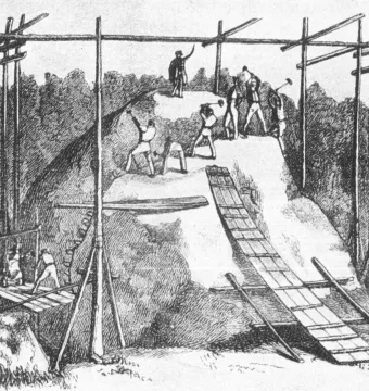 Historical engraving of men cutting a large granite bowl-shaped stone with hand tools and wooden scaffolding.