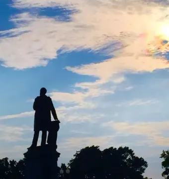 James A. Garfield Monument silhouetted against a colorful sunset sky with dark trees below.