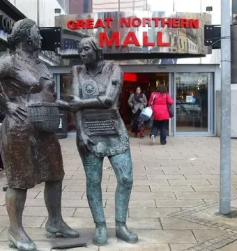 Monument to the Unknown Woman Worker with two bronze women standing outside a shopping mall entrance.