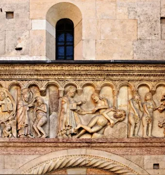 Stone bas-relief from Scenes from Genesis showing biblical figures beneath small arches, including a central seated figure in a mandorla and Adam and Eve by a twisted tree with a serpent.