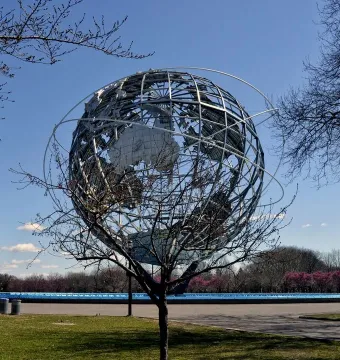 The Unisphere metal globe sculpture with orbital rings against a blue sky, framed by bare branches.