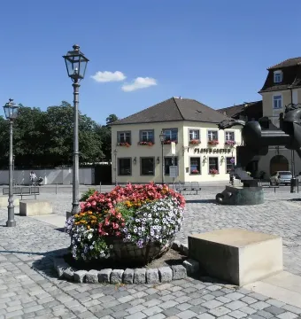 Anscavallo, a large abstract equine sculpture on a paved square with flower planters and streetlamps nearby.