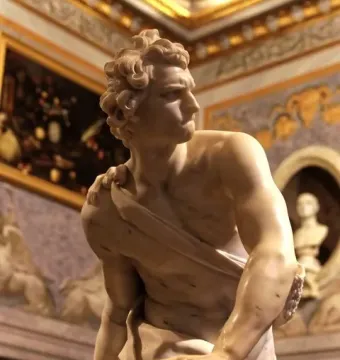 Bernini\'s David marble statue shown in a gallery interior, holding a sling and looking to the side.