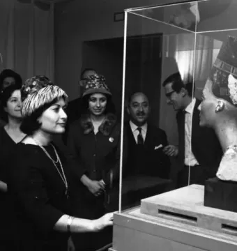 Bust of Nefertiti displayed in a glass case, with visitors gathered around it.