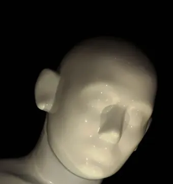 Close-up of Greetingman showing a bowed head and upper torso against a black background.