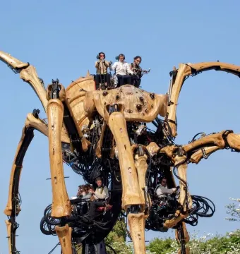 La Princesse, a giant mechanical spider with segmented legs and people operating it beneath a blue sky.