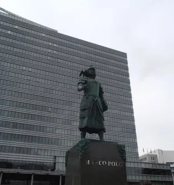 Marco Polo statue on a stone pedestal in front of a modern building.