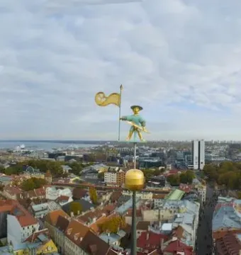 Old Thomas weathervane above Tallinn’s skyline with historic rooftops and modern buildings in the distance.