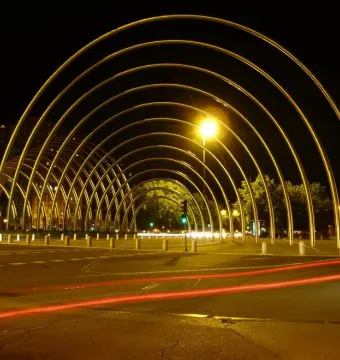 Puerta de la Ilustración lit with golden arches curving into a tunnel-like structure at night, with red light trails on the pavement.