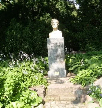 Bust of Stanisław Wyspiański on a dark pedestal in a green garden