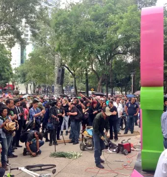 Antimonumento 49 ABC in a public plaza, with people photographing and filming as someone uses power tools at its base.