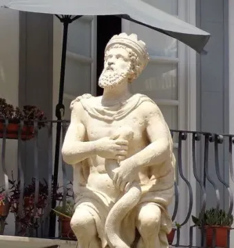 The Fountain of the Genius of Fieravecchia shows a crowned bearded stone figure holding a snake above a mossy fountain basin.
