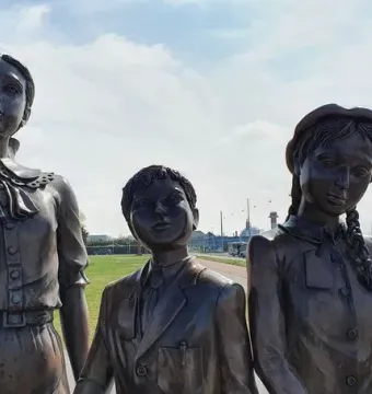 Kindertransport bronze sculpture of three children standing outdoors near a road and grassy area.