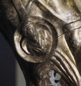 Close-up of the Waldgirmes Horse\'s Head showing a bronze-toned circular medallion with a profile head and decorative folds around it.