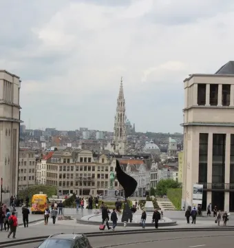 The Whirling Ear sculpture in a circular plaza with people walking nearby and a city skyline in the background.