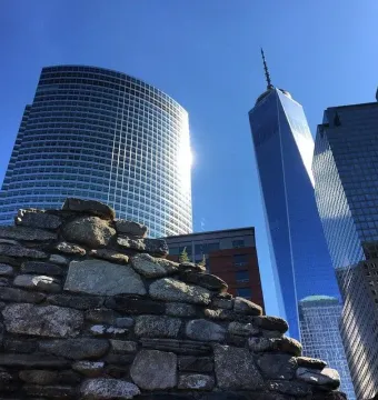 Irish Hunger Memorial stone wall in front of modern Manhattan skyscrapers under a clear blue sky.