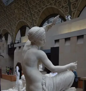 Jeune fille de Mégare, a white marble sculpture of a seated young woman holding a spindle and distaff