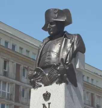 Bronze bust of Napoleon I on a tall stone plinth decorated with eagles, a crown, and the letter N.