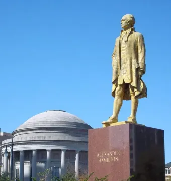 Alexander Hamilton statue on a stone pedestal with a domed classical building in the background