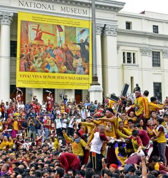 The Black Nazarene statue is carried on a platform through a dense crowd, with people reaching out toward it.