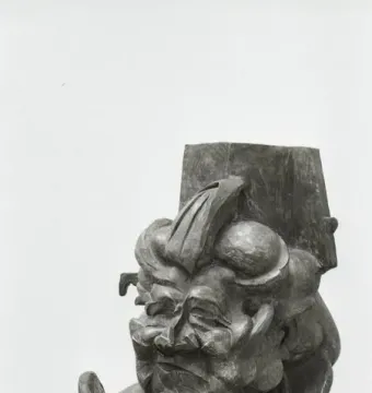 L\'antigrazioso bust with fragmented, distorted facial features on a dark slatted base.