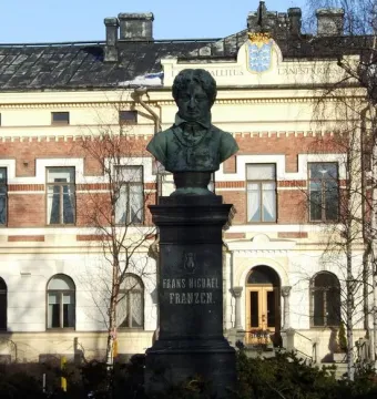 Frans Michael Franzén statue on a tall stone pedestal with a historic building and bare trees behind it.