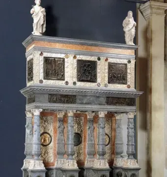 Martinengo Mausoleum with a lower tier of slender carved columns, rectangular relief panels, and two white stone figures on the top surface.