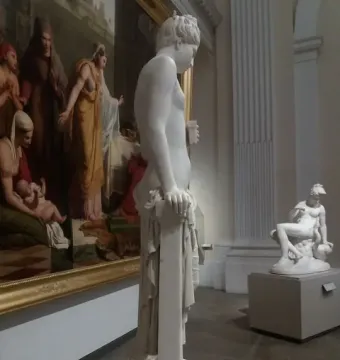Pandora marble statue in profile, holding a small object beside a draped pillar.