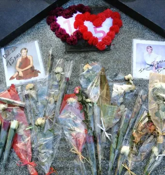 A memorial on a dark granite surface with wrapped bouquets, two framed photos of Princess Diana, and a heart-shaped floral wreath marked 15.