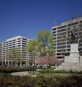 Admiral David G. Farragut statue on a stone pedestal in a park setting with trees, fencing, and buildings behind it.
