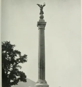 Battle Monument with a tall column topped by a winged female figure holding a wreath aloft, standing on a stepped base with smaller surrounding pedestals.