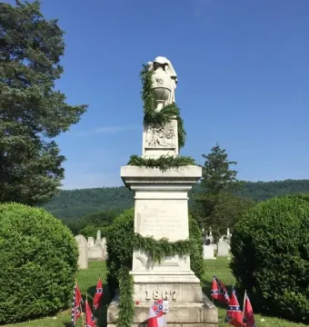 Confederate Memorial stone monument topped by an urn, with green garland and small Confederate flags around the base.
