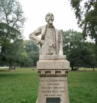 Busto of Ernesto Teodoro Moneta on a tall inscribed pedestal in a grassy park.