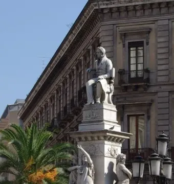 Monument to Vincenzo Bellini with a seated figure atop a marble pedestal and allegorical statues below.