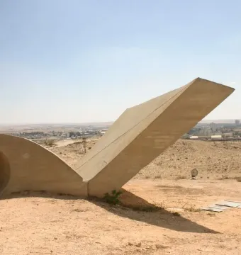 Monument to the Negev Brigade, a large abstract concrete sculpture on a sandy hillside with a city in the distance.