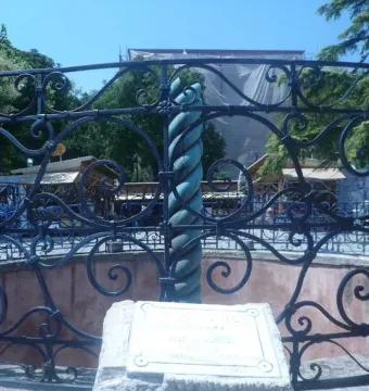 A section of the Serpent Column beside an ornate black wrought-iron fence, with a stone plaque block in the foreground.