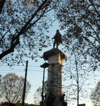 Monument to Vittorio Emanuele II seen from below, with a statue atop an ornate column against a blue sky.