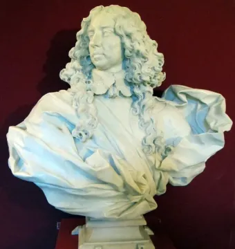 White marble bust of Francesco I d\'Este with curly hair, an ornate lace collar, and a draped garment against a red wall.