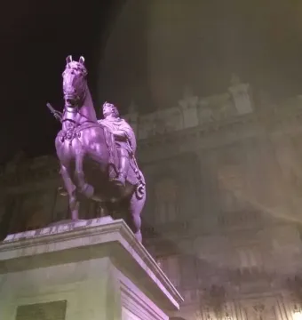 El Caballito equestrian statue lit in purple at night on a tall stone pedestal, with an ornate building behind it.