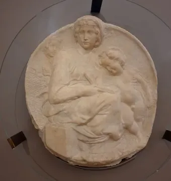 Michelangelo’s Pitti Tondo relief sculpture showing the Madonna and Child with the young Saint John behind glass.
