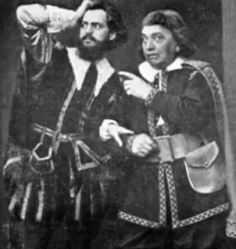 Two actors in elaborate stage costumes from The Stone Guest, one bearded man holding a hand to his head while the other points with both hands.