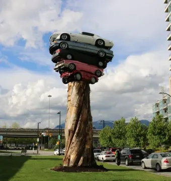 Trans Am Rapture sculpture with five cars stacked on a tall wooden column in a grassy urban setting