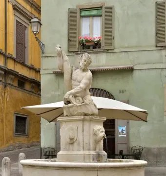Dolphin Fountain with Triton, a stone sculpture of a bearded man holding a fish in a cobblestone square.